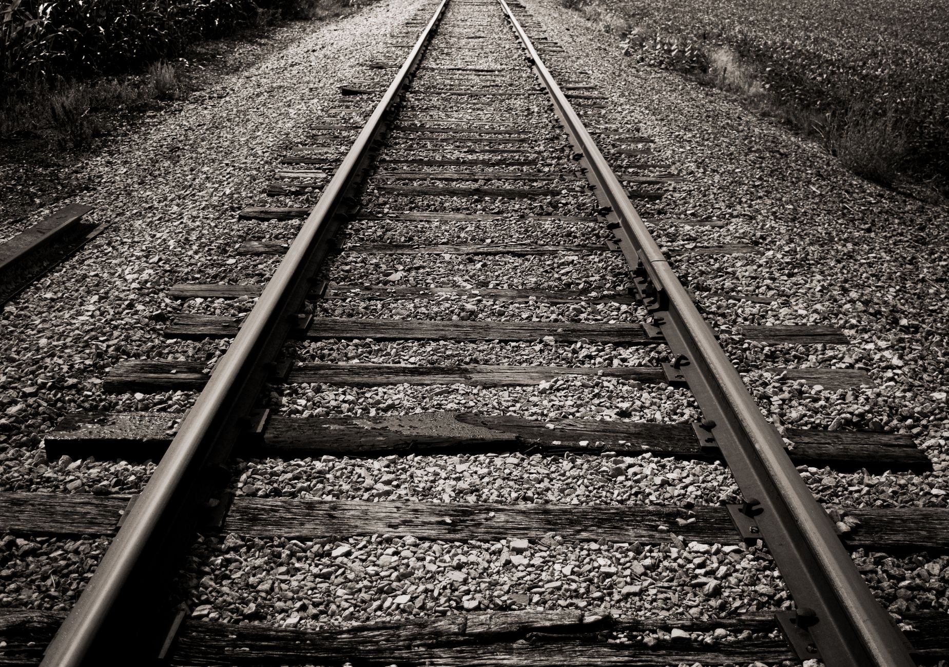 Black and white photo of rustic railroad tracks disappearing into the distance.