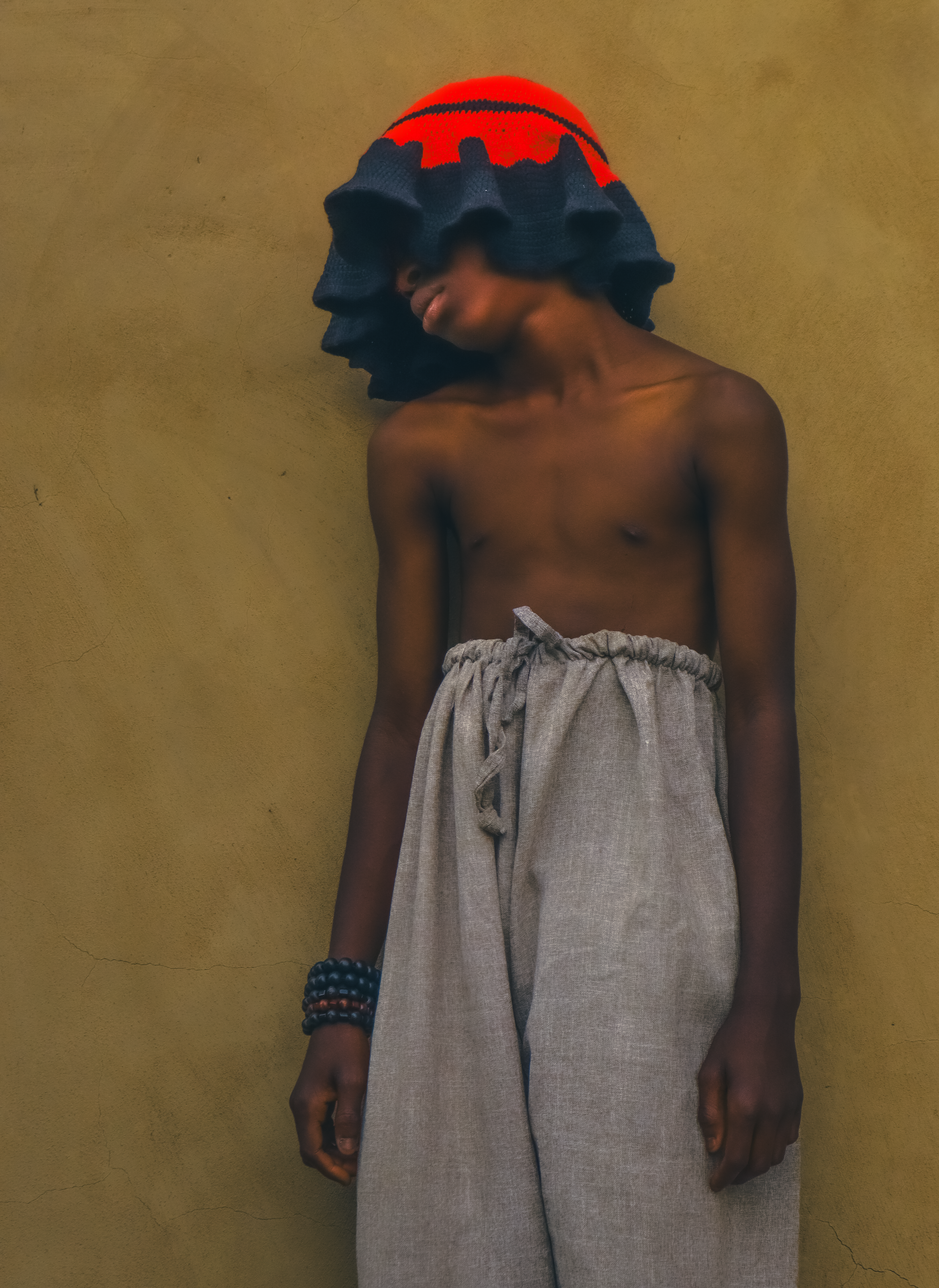 A young man wearing traditional Nigerian attire with a colorful hat against a plain background.