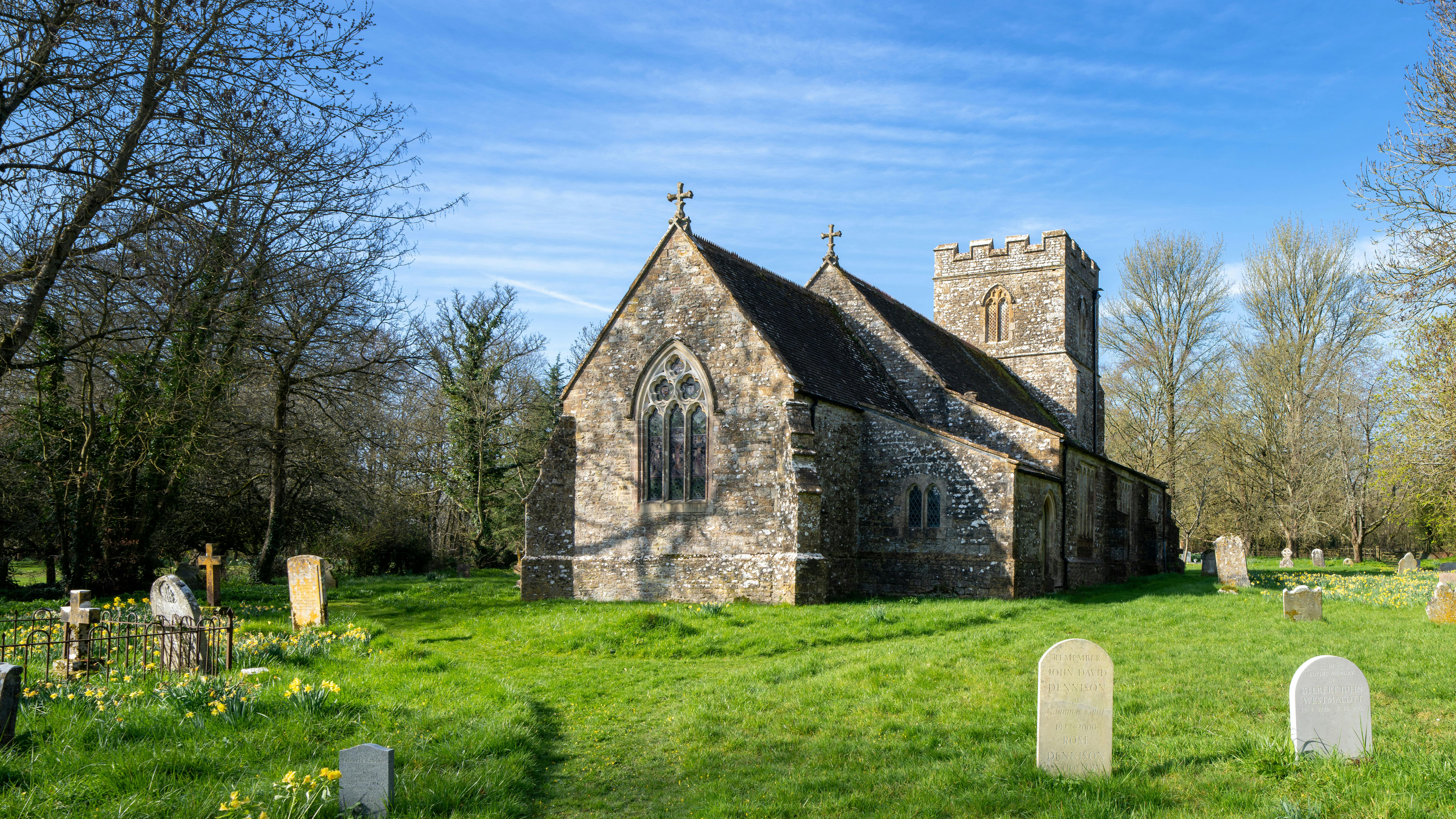 A tranquil stone church in Dorset surrounded by greenery and gravestones.