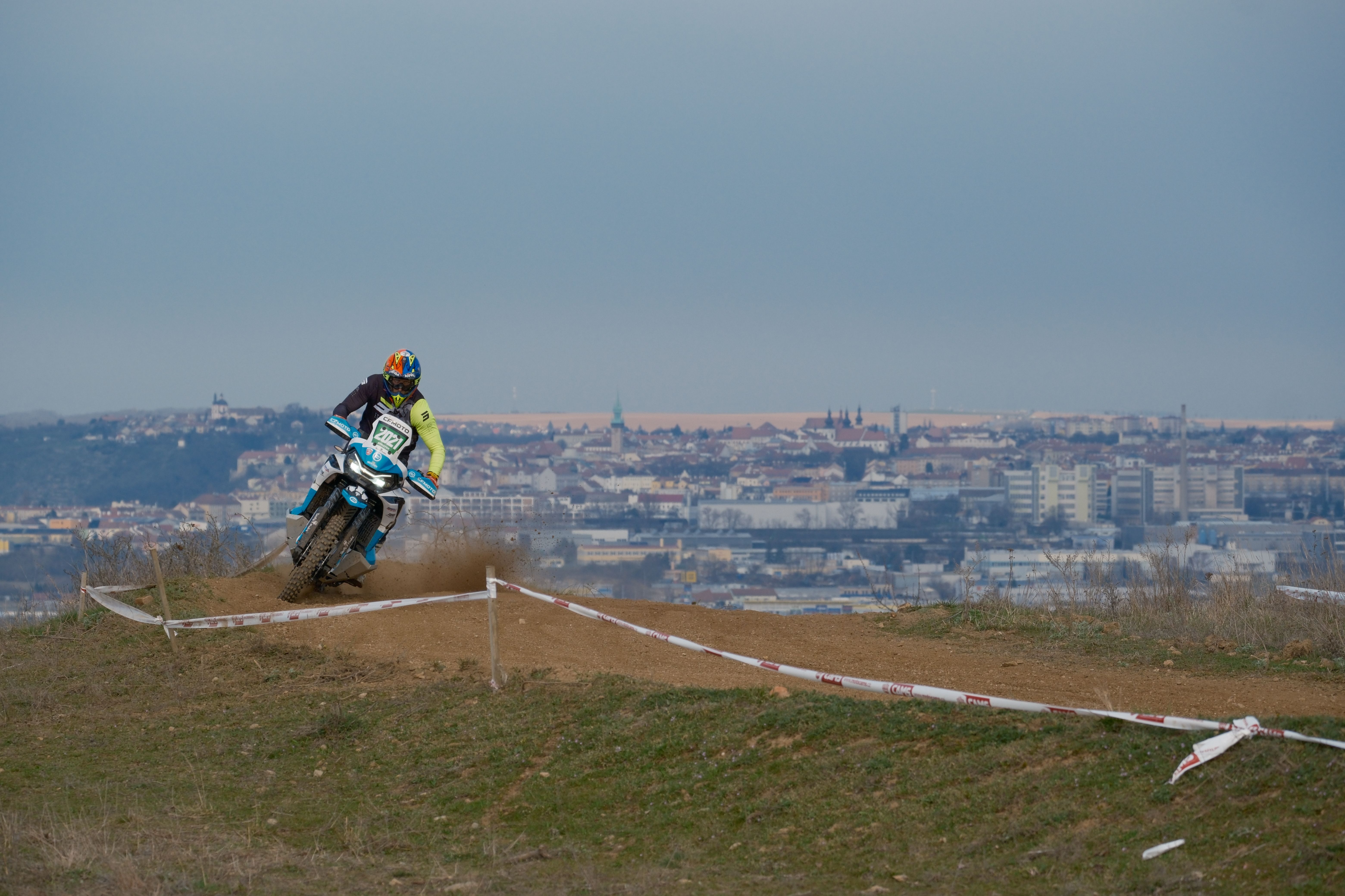 Exciting motocross action on a dirt track with Jihomoravský Kraj skyline in the background.
