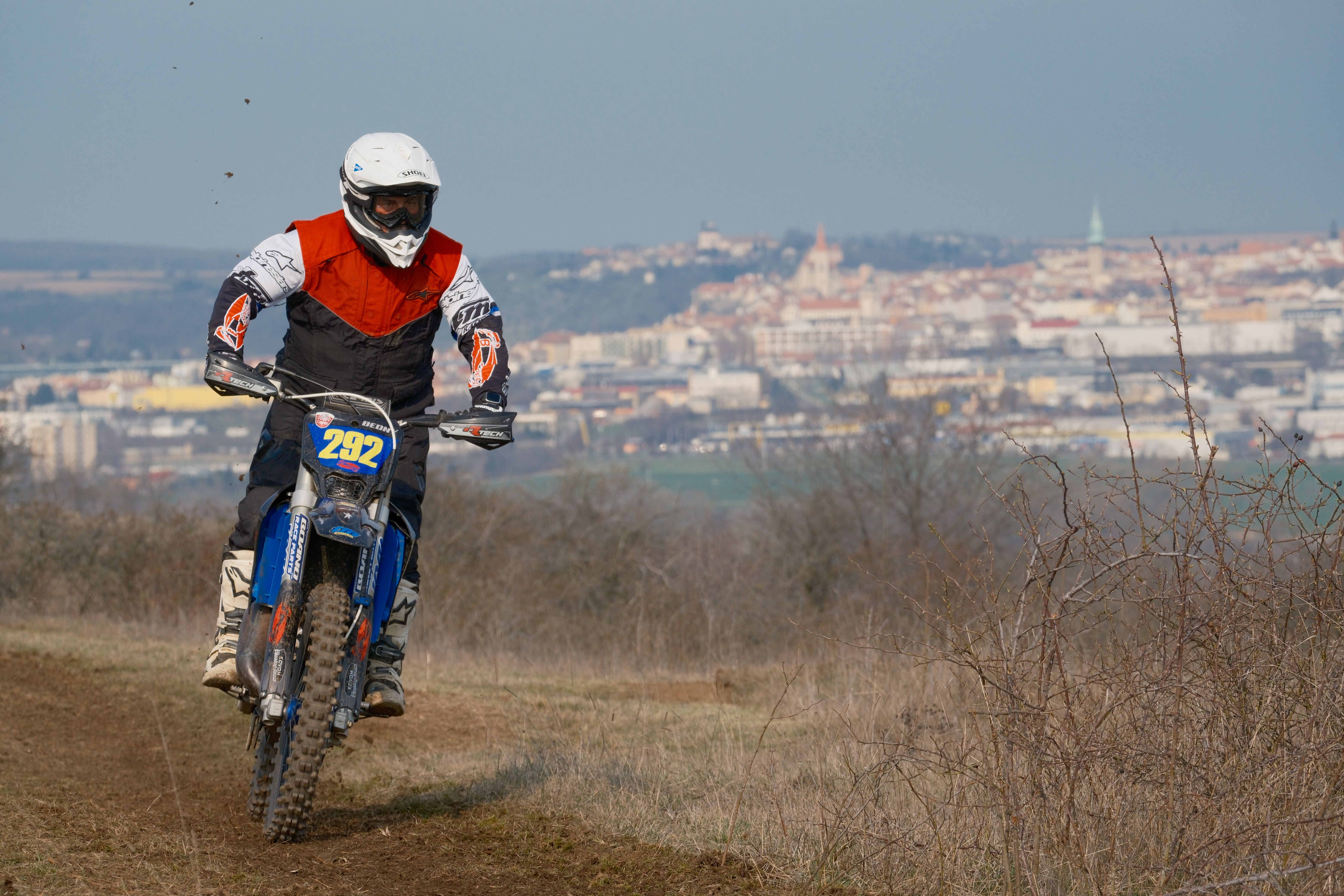 A motorcyclist rides off-road with a cityscape in the background in Jihomoravský kraj.