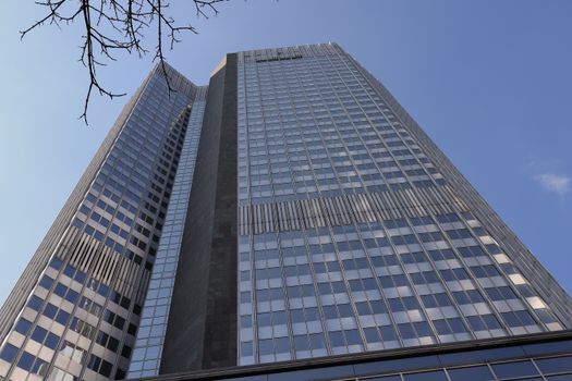 A towering skyscraper in the heart of Frankfurt's financial district against a clear blue sky.