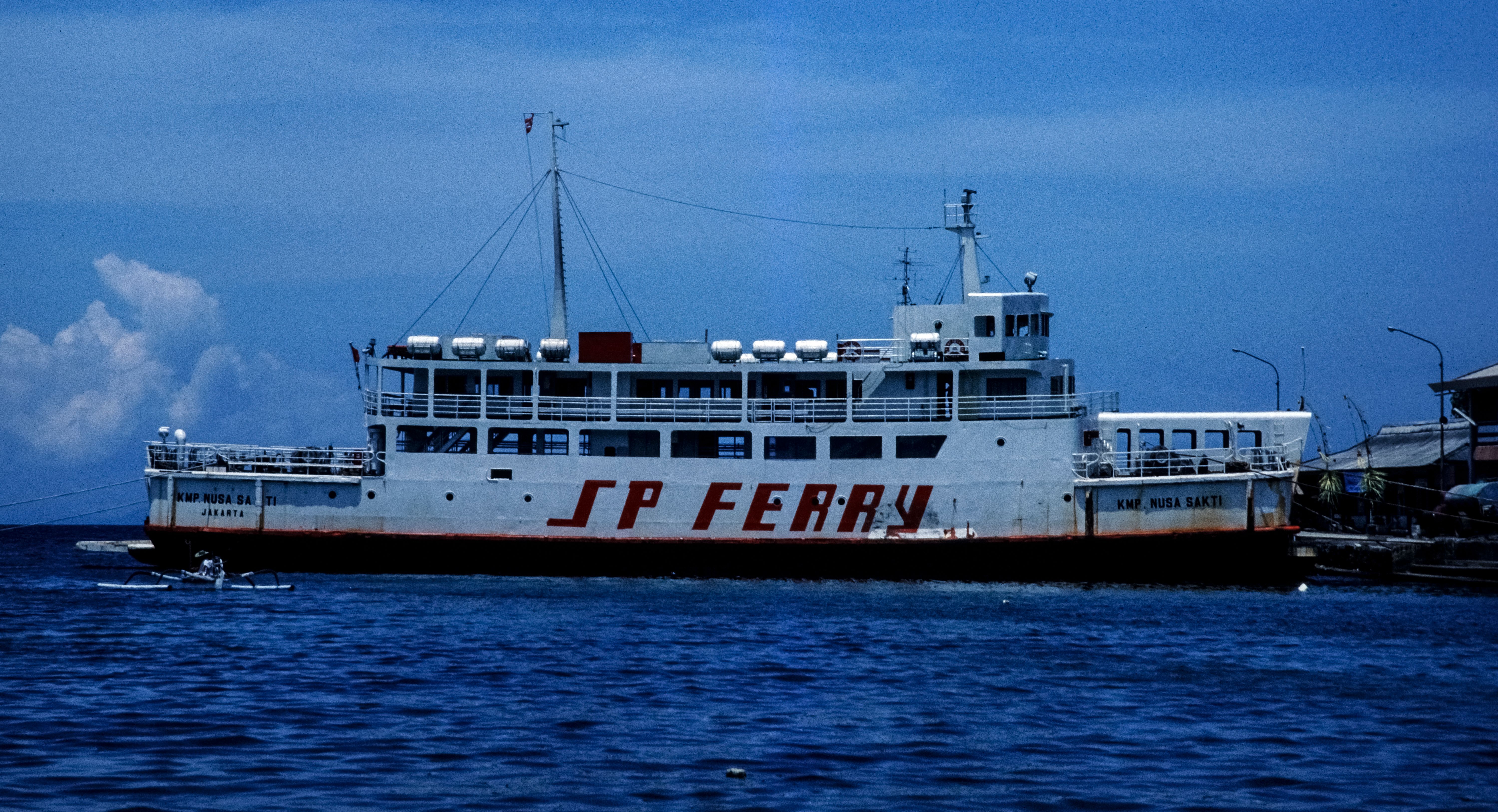 A large ferry named SP Ferry docked at the shore in Indonesia under a clear blue sky.