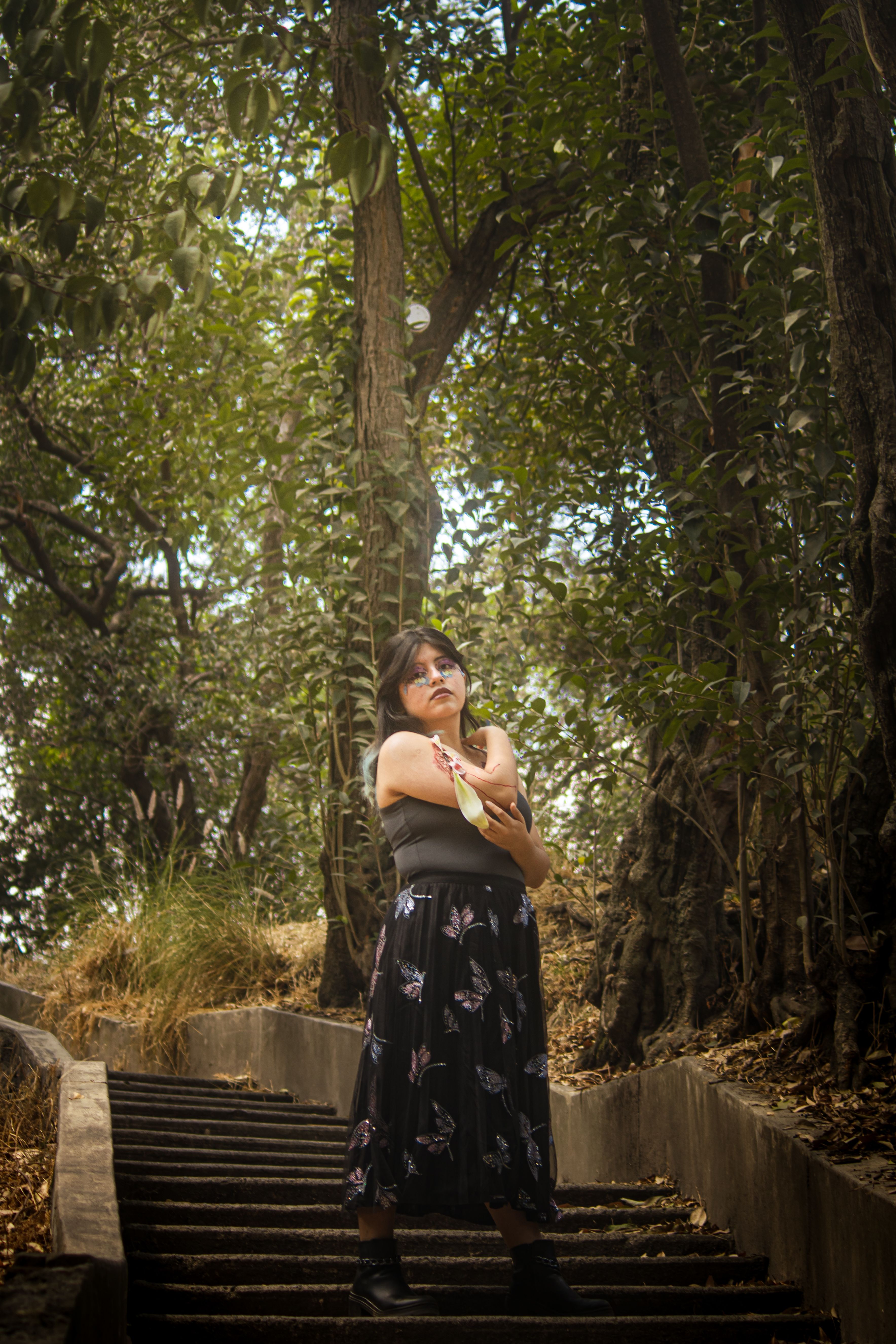 A woman poses on park stairs surrounded by lush greenery in Mexico City, showcasing floral fashion.