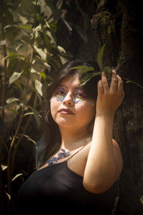 Free A woman with artistic makeup and floral accessories poses gracefully in a forest setting. Stock Photo
