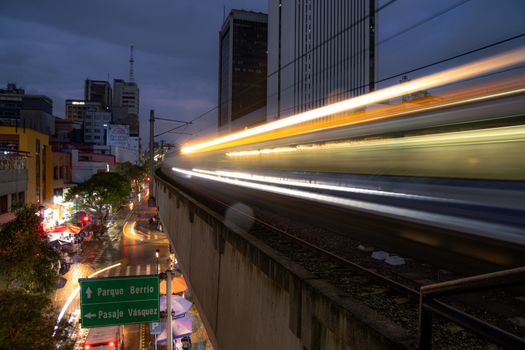 Long exposure capture of a train moving through Medellín at night, showcasing urban life and speed.