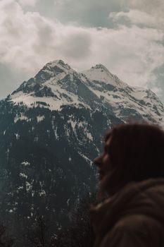 Silhouette of person in front of majestic snow-capped mountains under cloudy sky.
