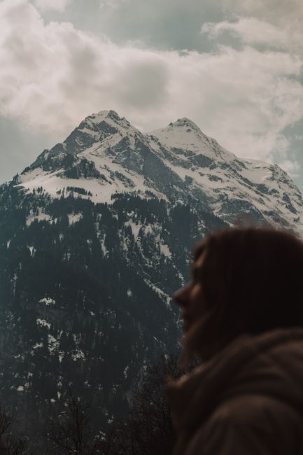 Silhouette of person in front of majestic snow-capped mountains under cloudy sky.