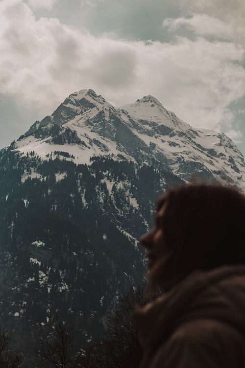 Free Silhouette of person in front of majestic snow-capped mountains under cloudy sky. Stock Photo