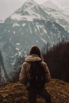 Traveler with backpack enjoying majestic snow-capped mountain views on a cloudy day.