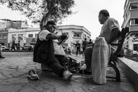 A shoe shiner works on a client's shoes in a vibrant street scene in Trujillo, Peru.