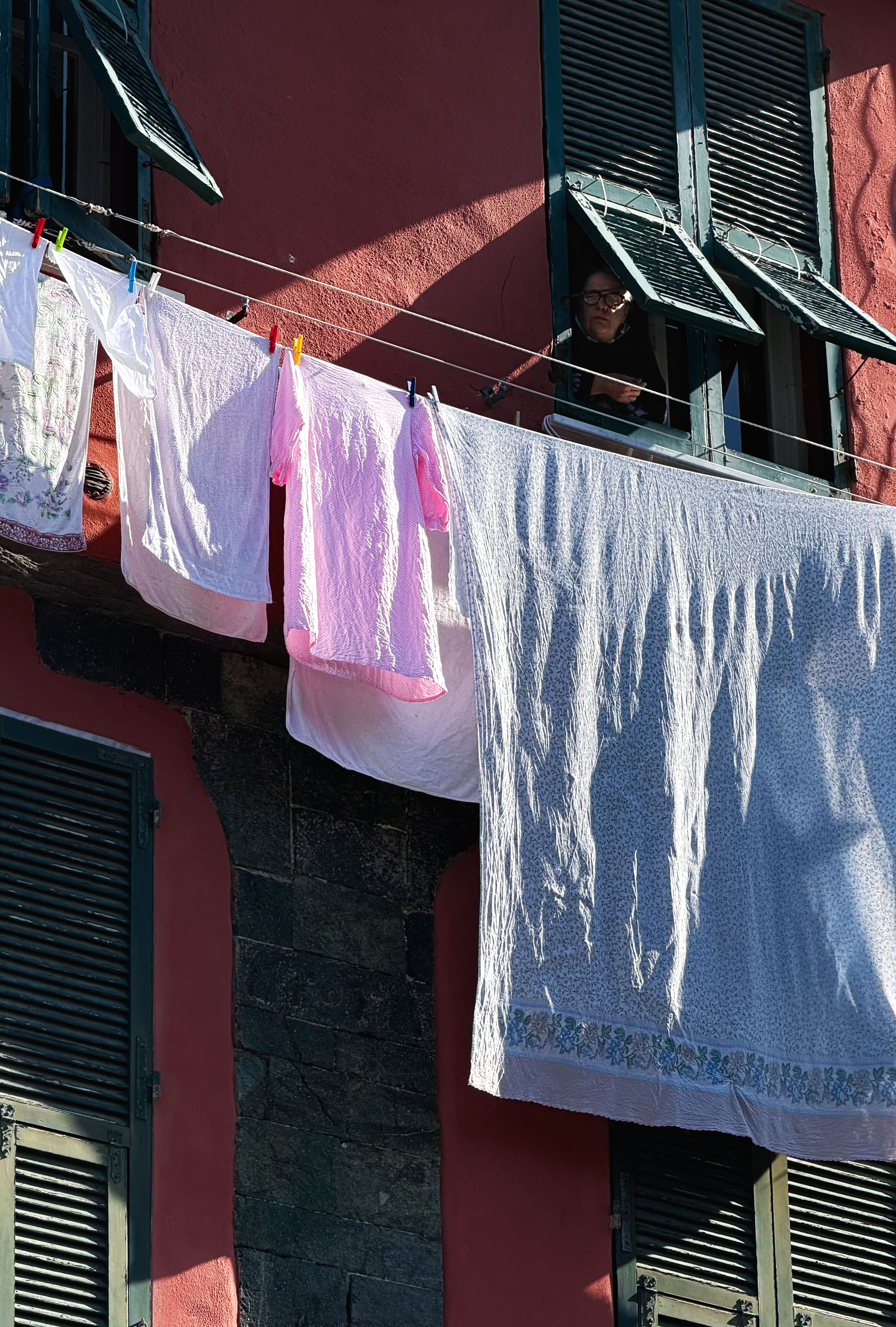 Colorful laundry hanging outside a typical Italian house with green shutters on a sunny day.