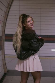 Young woman with long hair posing in a dimly lit subway station, exuding modern street style.