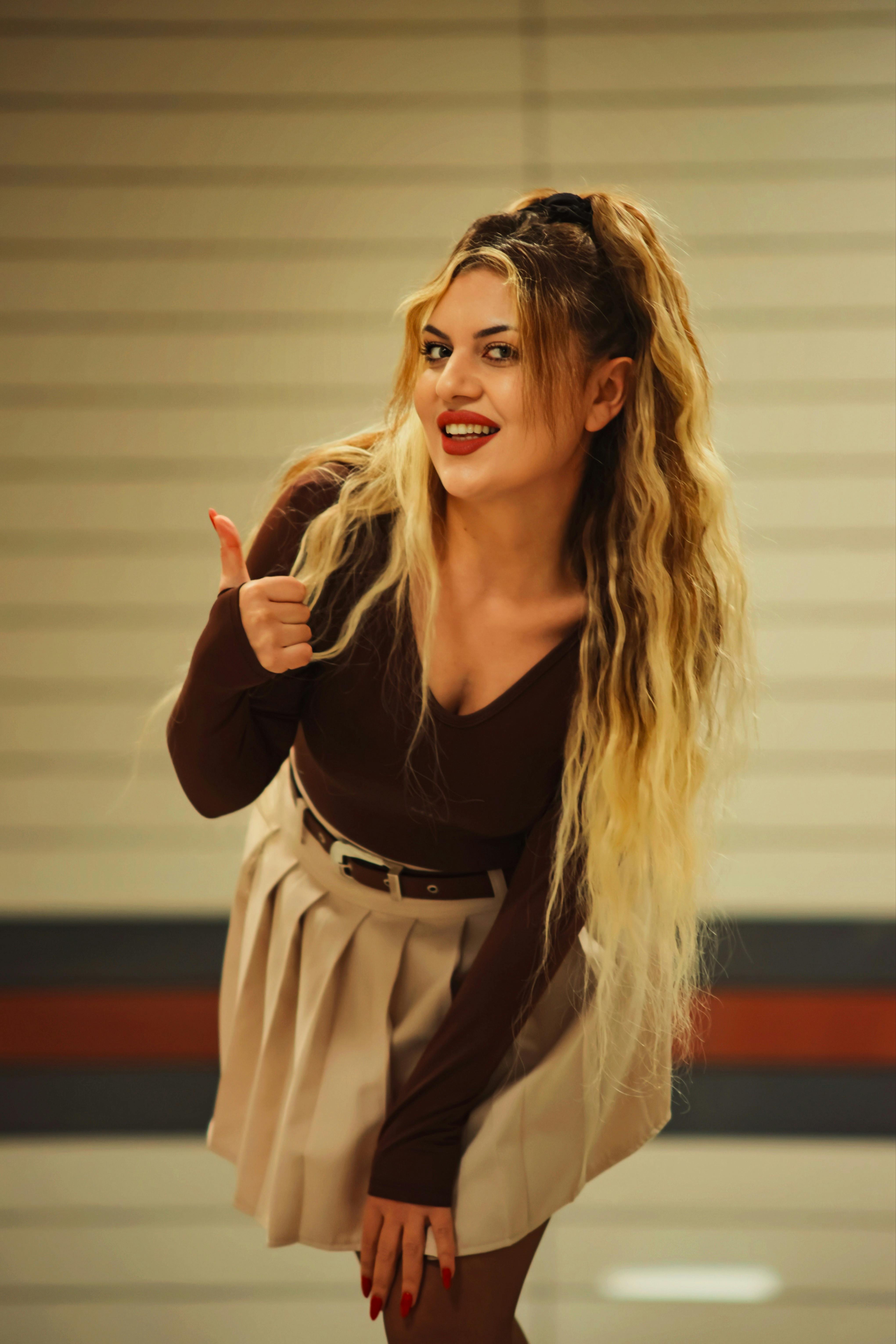 Smiling woman with long hair offering a thumbs up gesture inside a building.