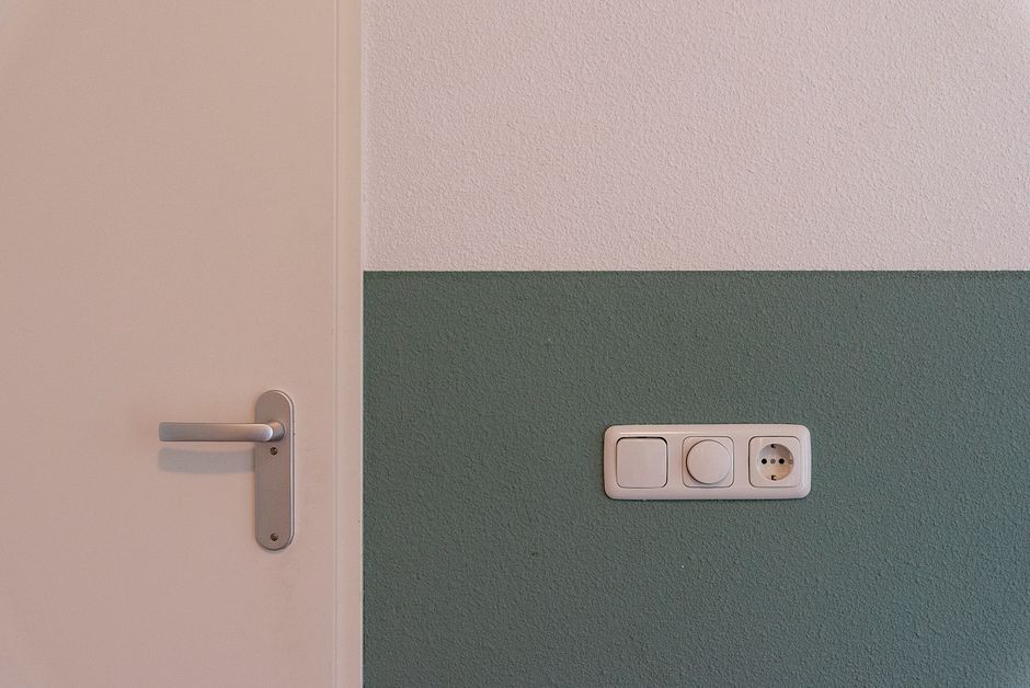 Ściana salonu z gniazdkiem elektrycznym, wykończenie w szarościach, miejsce potencjalnych nieszczelności akustycznych