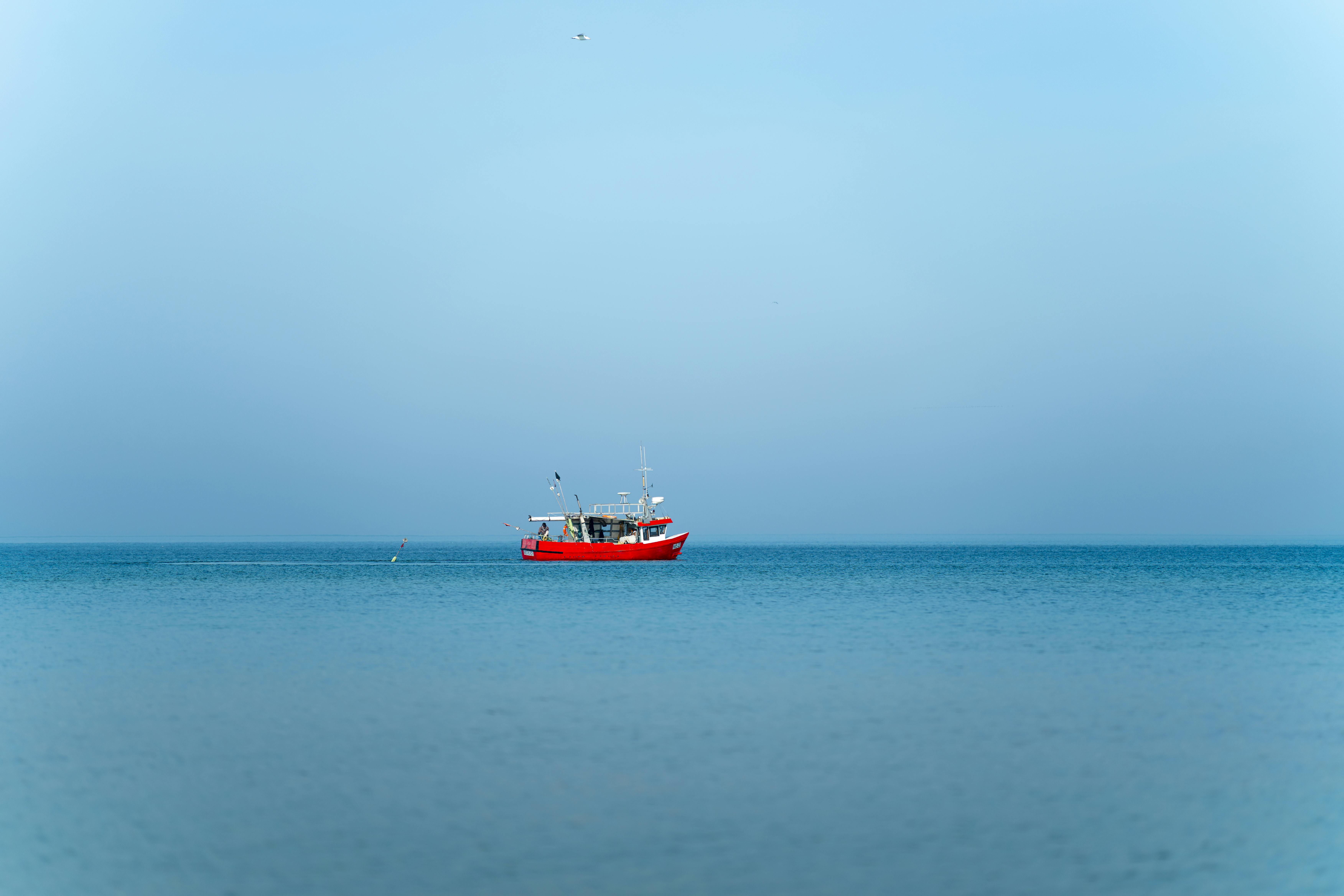 Gratuit Scène paisible d'un bateau rouge flottant sur une mer calme sous un ciel bleu clair près de Kołobrzeg, en Pologne. Photos
