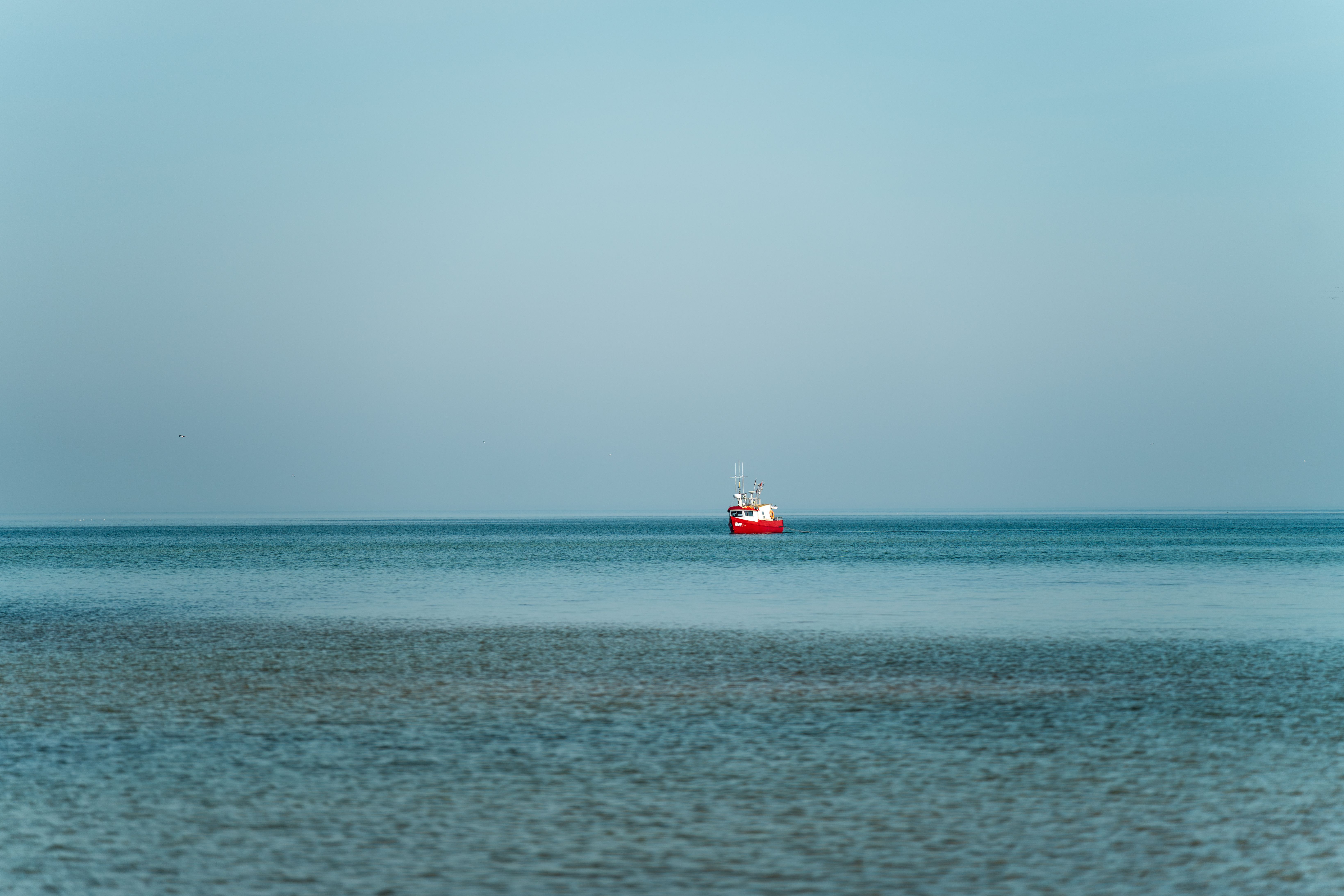 A lone red fishing boat floats on the serene waters of the Baltic Sea in Kołobrzeg, Poland. — Trójmiasto