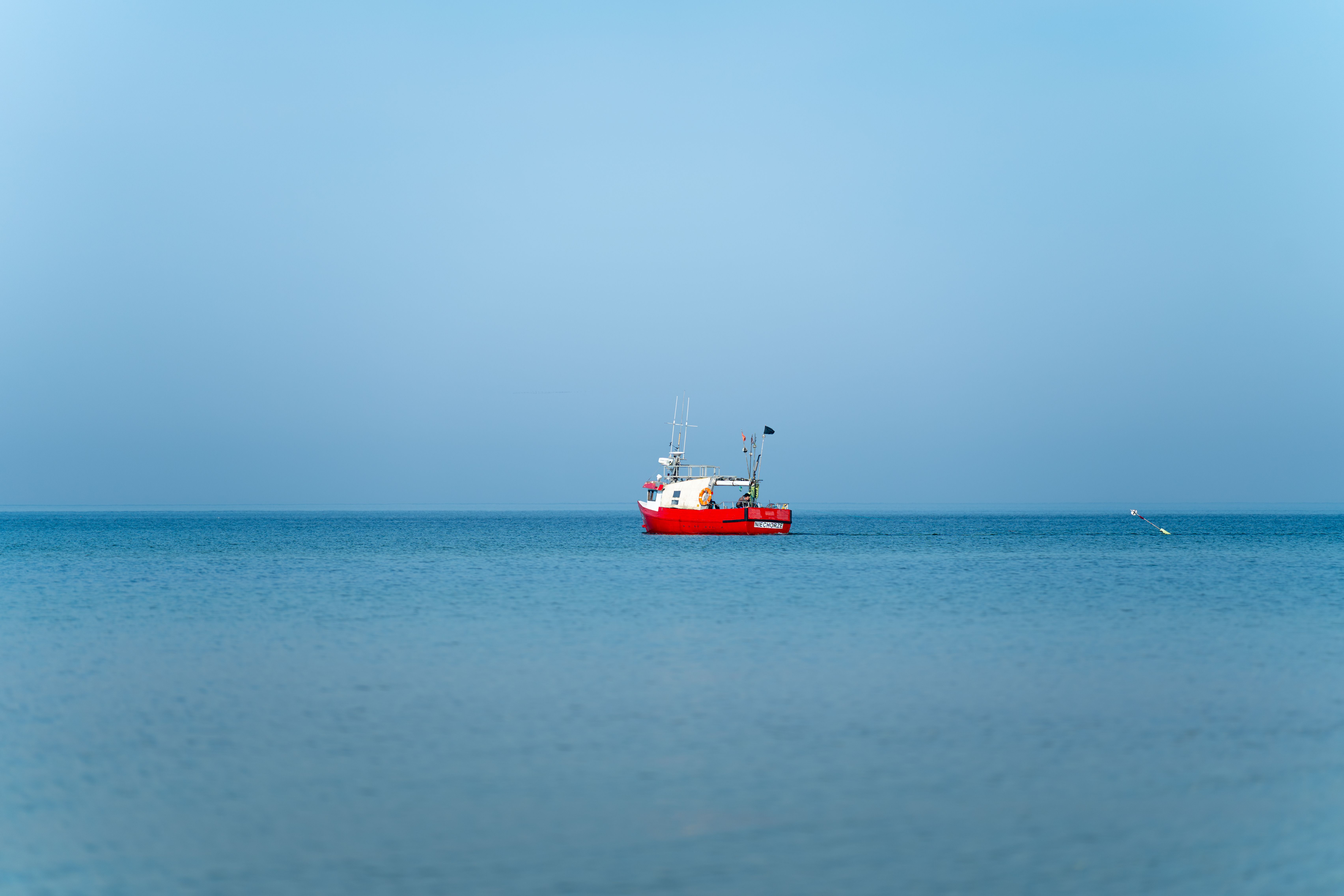 Gratuit Un bateau de pêche rouge vif flotte paisiblement sur la mer Baltique calme, près de Kołobrzeg, en Pologne. Photos