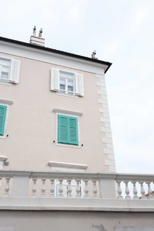 Free A minimalist facade featuring pastel green shutters on a beige building under a cloudy sky. Stock Photo