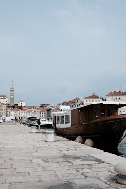 Free Historic harbor scene featuring a wooden boat and old town architecture under a clear sky. Stock Photo