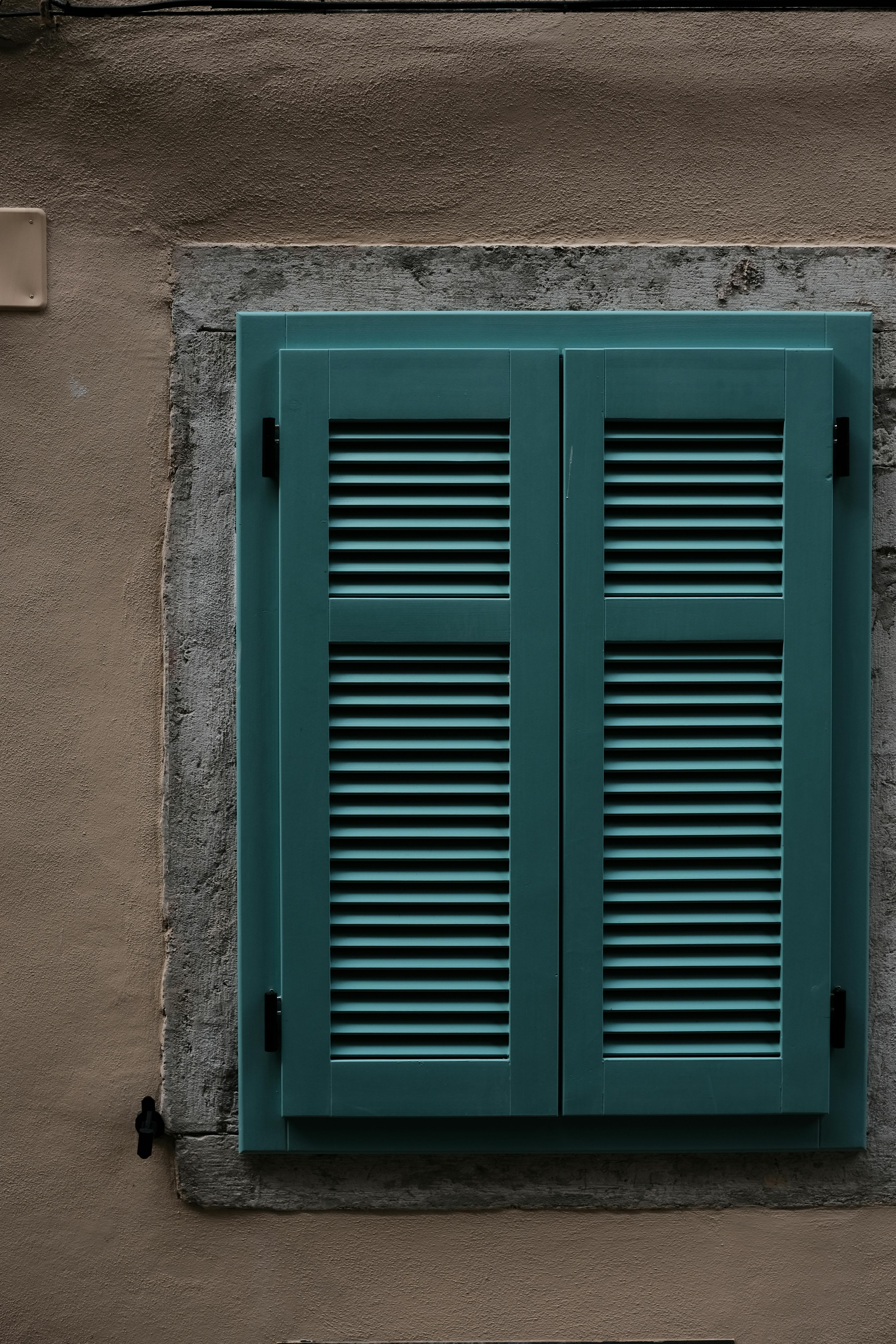 An artistic view of a teal shuttered window against a rustic textured wall, conveying a vintage charm.