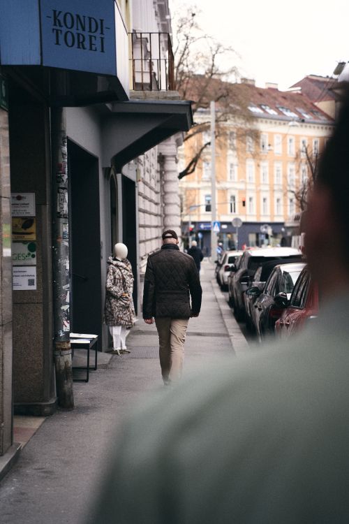 Free A city street view featuring two adults walking past a cafe, capturing daily urban life. Stock Photo
