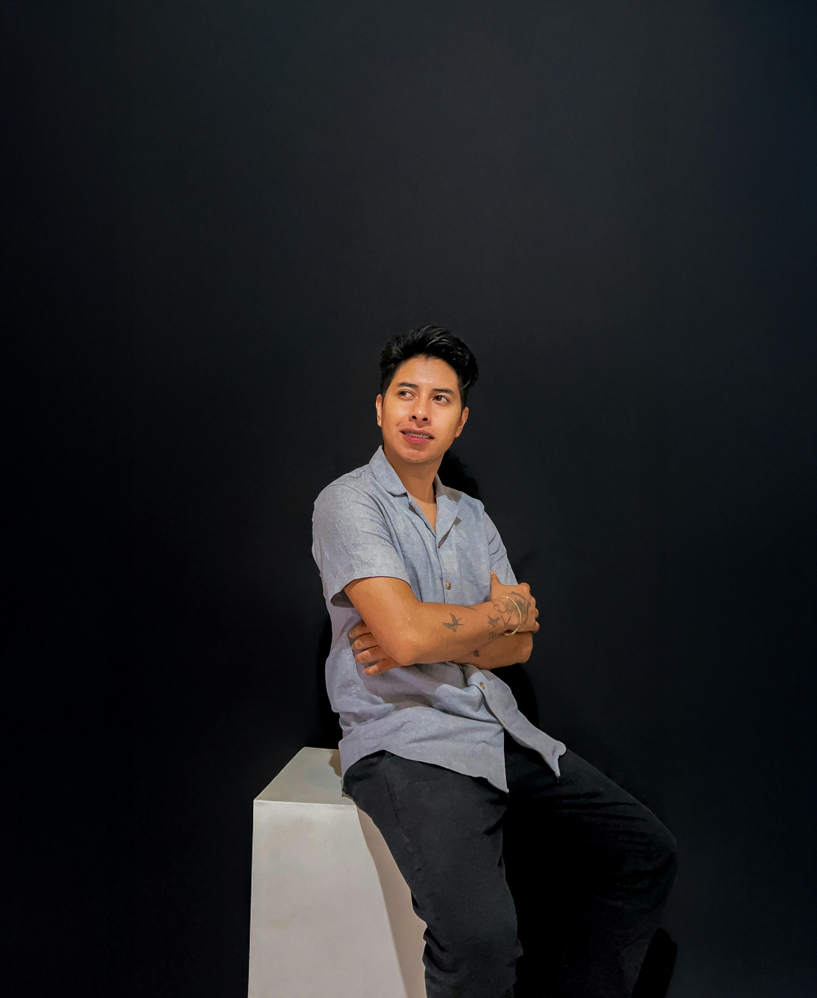 Thoughtful man sitting confidently on a stool against a dark background.