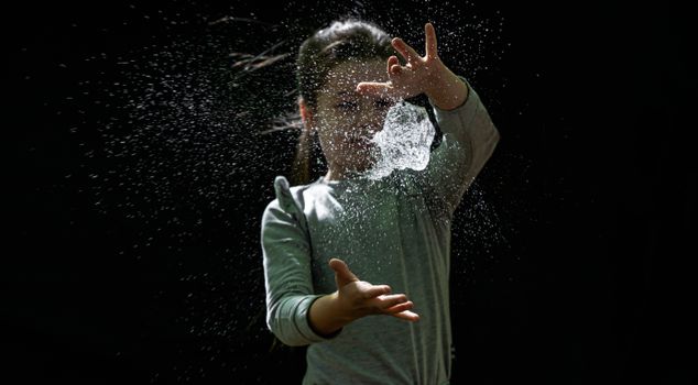 A young girl joyfully catching a splash of water in the air against a dark background.