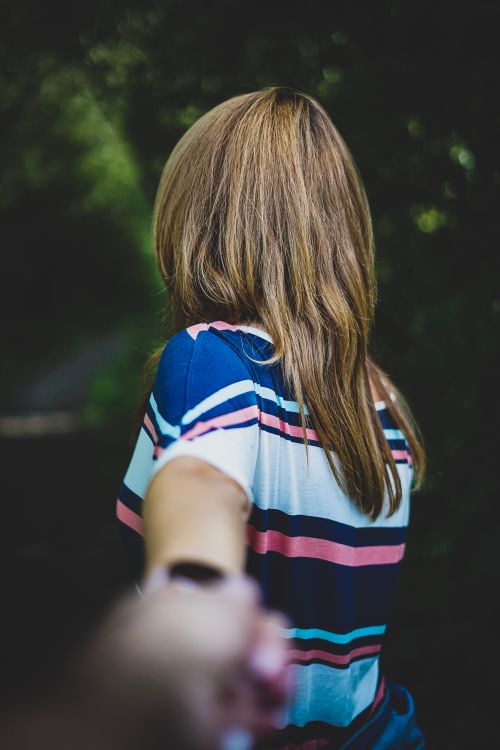 Free A woman leads through a lush path, holding hands with the photographer, creating a sense of connection and adventure. Stock Photo