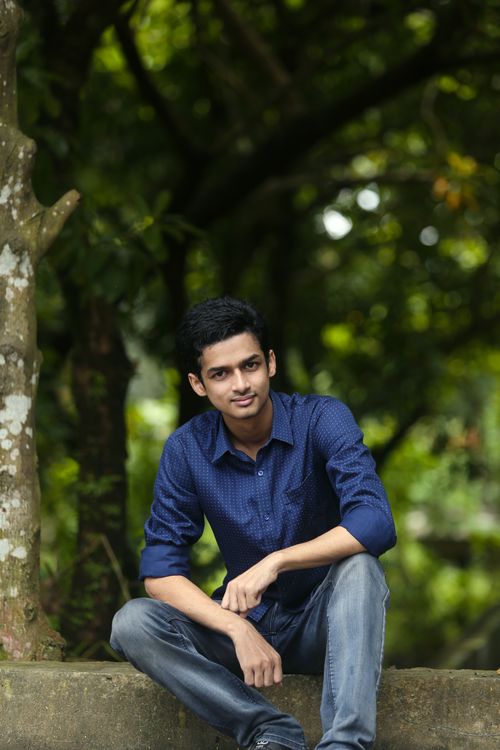Free A young man sitting casually outdoors in a lush green park, exuding calmness and serenity. Stock Photo