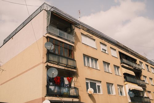 Free A residential building featuring balconies with satellite dishes against a cloudy sky. Stock Photo