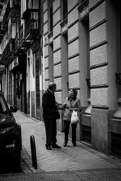 Gratuit Deux adultes qui discutent dans une rue de Madrid, un moment de vie urbaine spontané. Photos