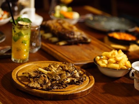 Delicious dinner setup featuring grilled mushrooms, crispy fries, and refreshing cocktail on wooden table.