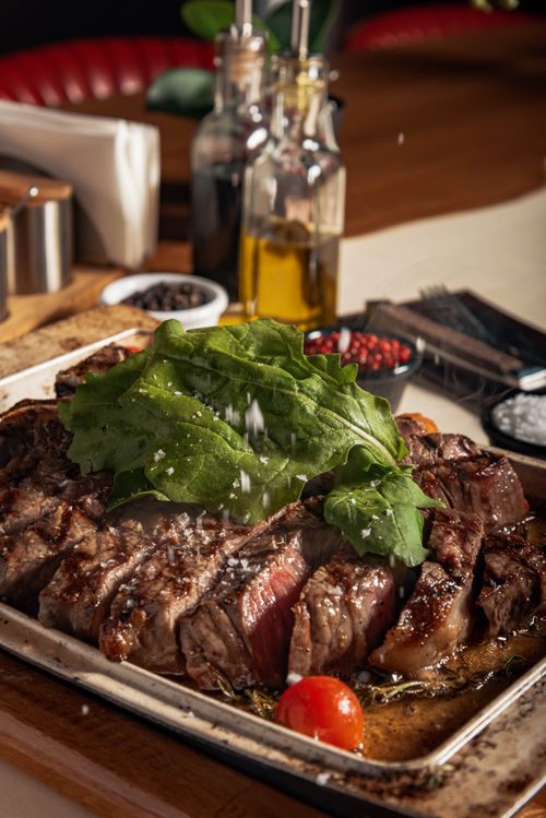 Free Juicy grilled beef steak topped with fresh greens and cherry tomatoes, perfect for a gourmet meal. Stock Photo