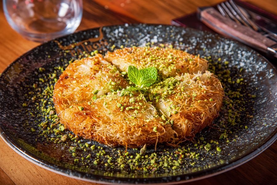 A round of golden kunafa covered in crushed pistachio with a sprig of mint