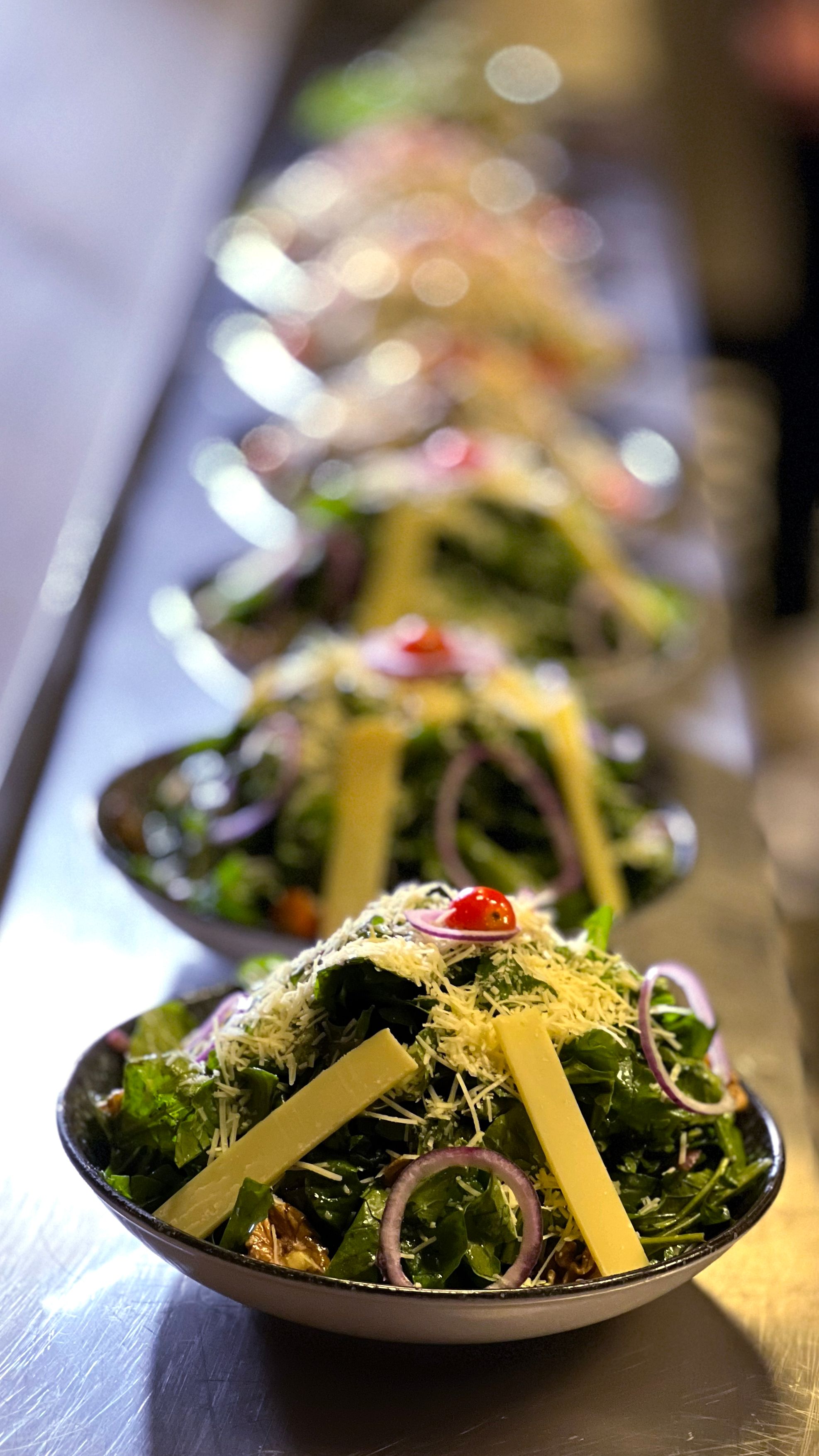Close-up of rows of fresh gourmet salads with cheese, onions, and cherry tomatoes, ready to serve.