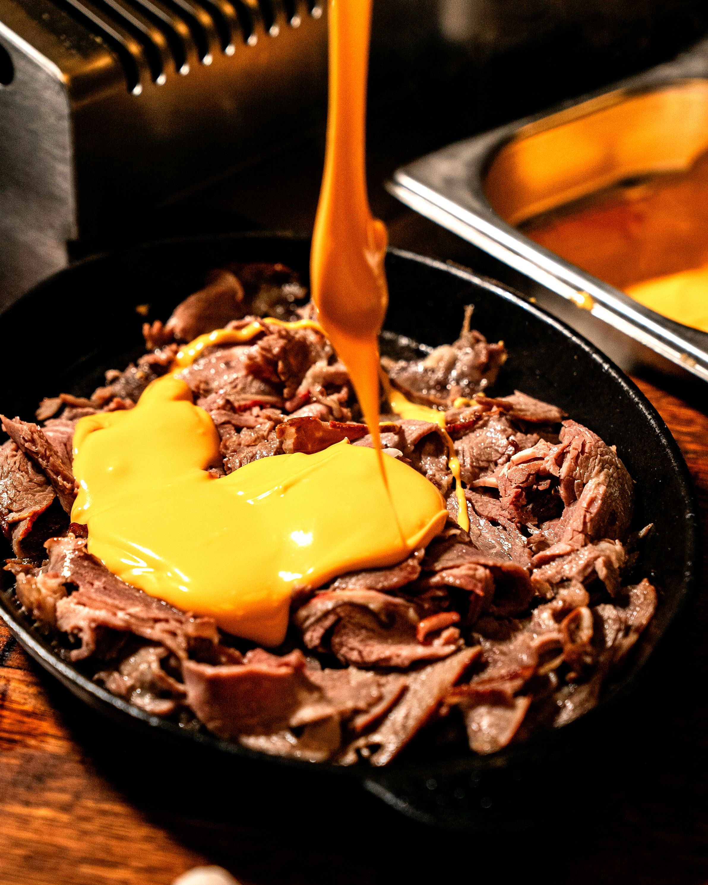 Two smash-style burger patties with a dark crust and melted cheddar sitting in a cast iron skillet, with a toasted bun beside them.
