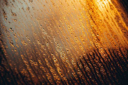 Abstract image of raindrops on glass during sunset, creating a golden, textured effect.