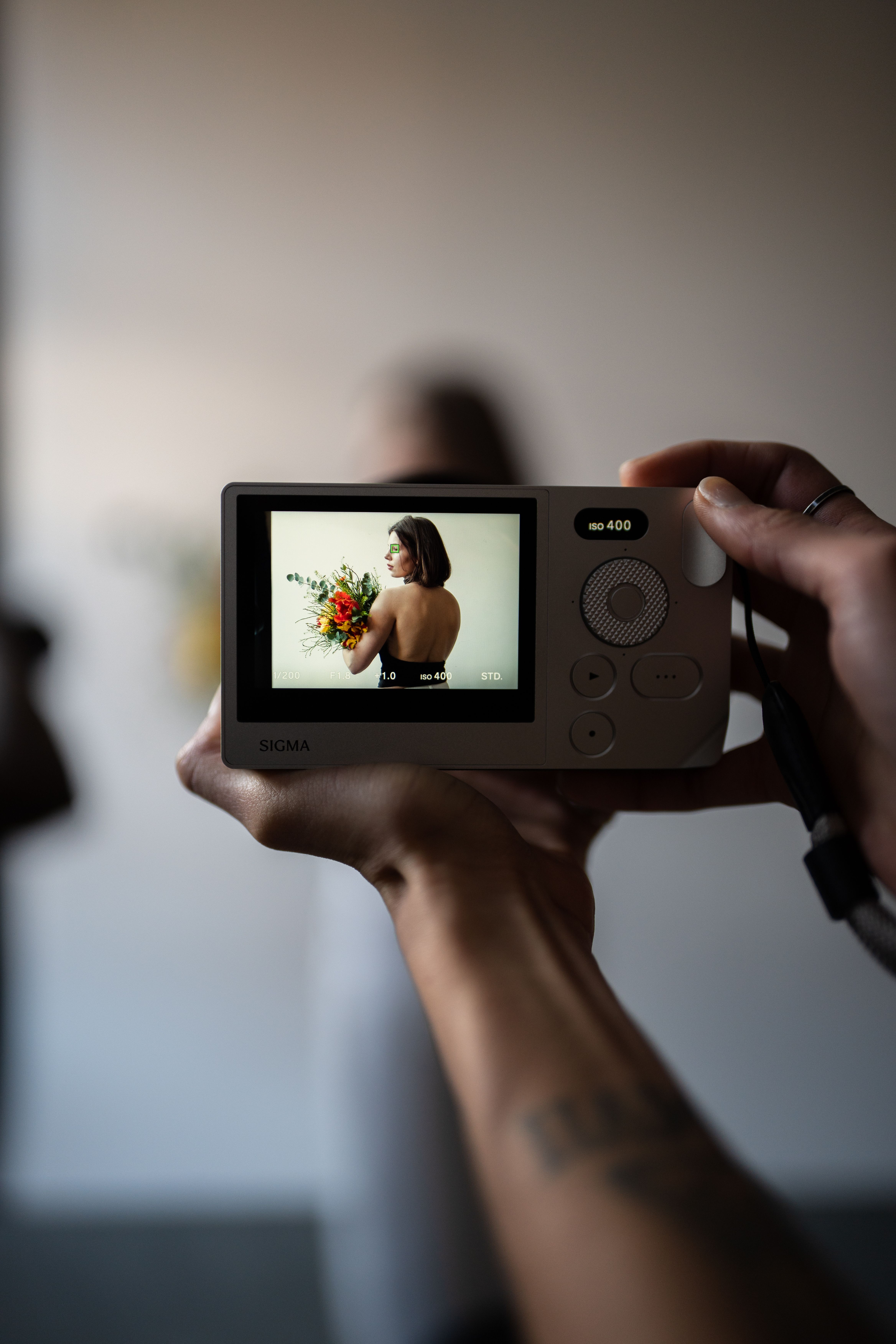 A person holding a camera showing a portrait on the display screen, capturing a model holding flowers.