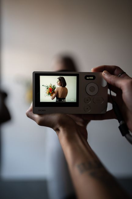 A person holding a camera showing a portrait on the display screen, capturing a model holding flowers.