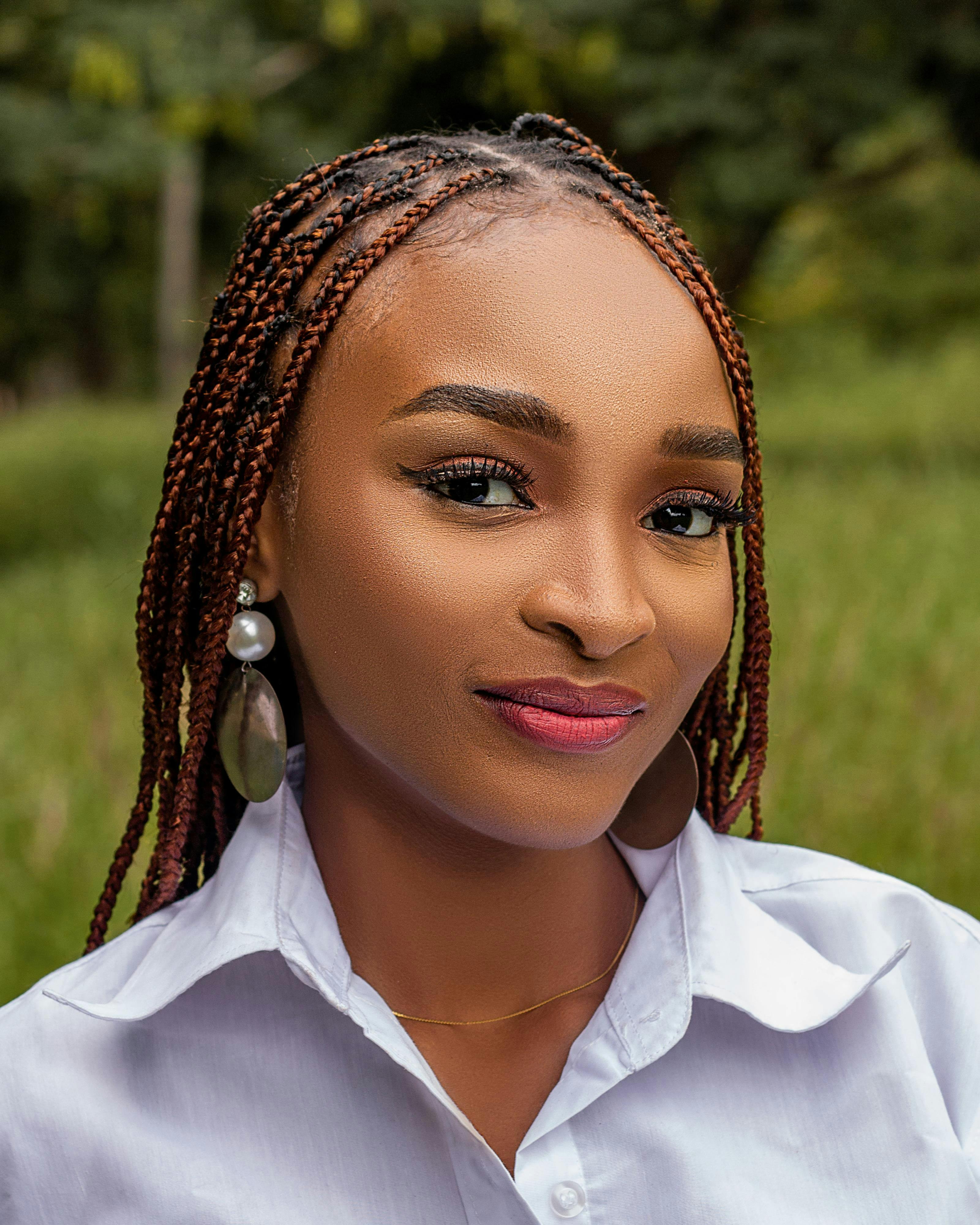 A vibrant portrait of a young woman with braided hair, smiling in a natural outdoor setting.