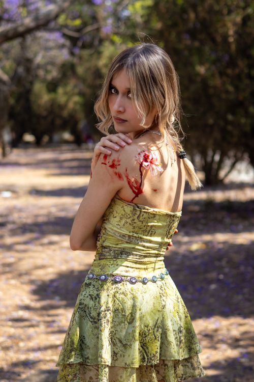 Free A woman in a green dress with a blood effect on her shoulder, posing outside. Stock Photo