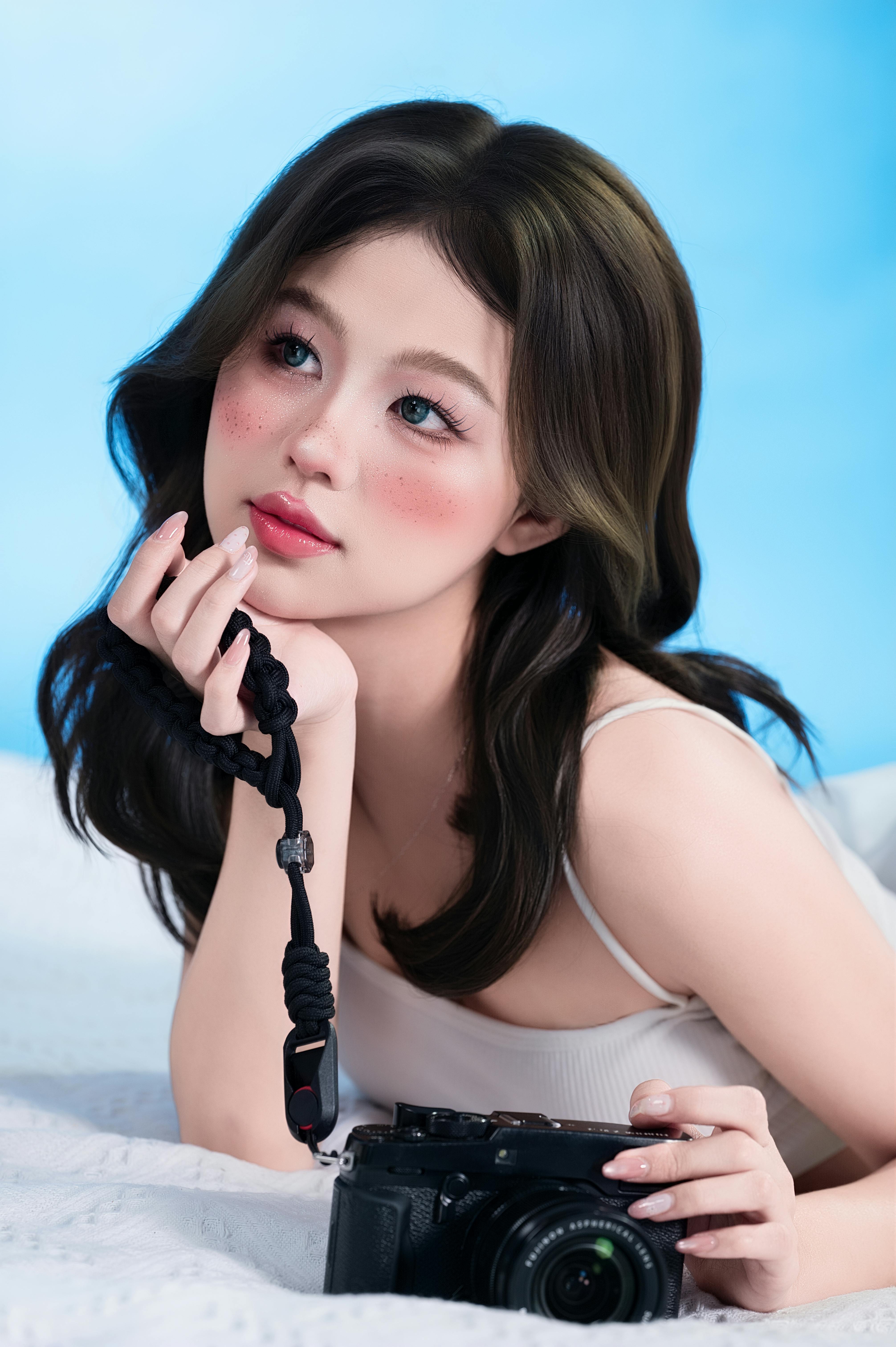 Charming young woman holding a camera, posing in a studio with a soft blue background.