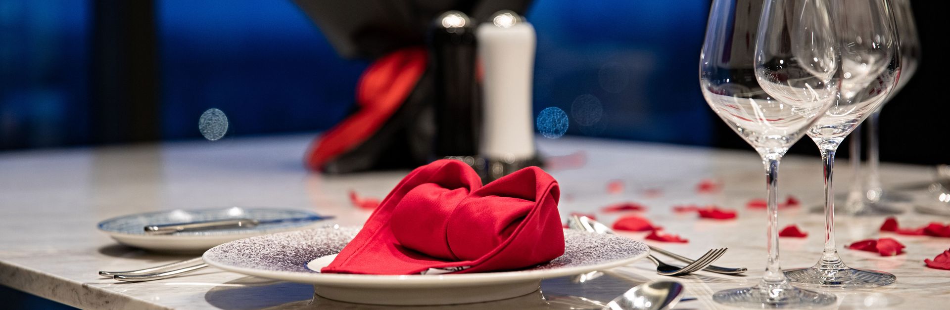 Elegant romantic dinner setting with red roses petals and folded napkin, perfect for special occasio