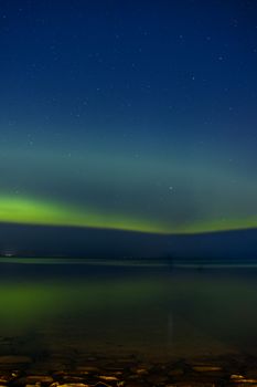 Beautiful northern lights reflected over a lake in Jönköping, Sweden under a starry night sky.