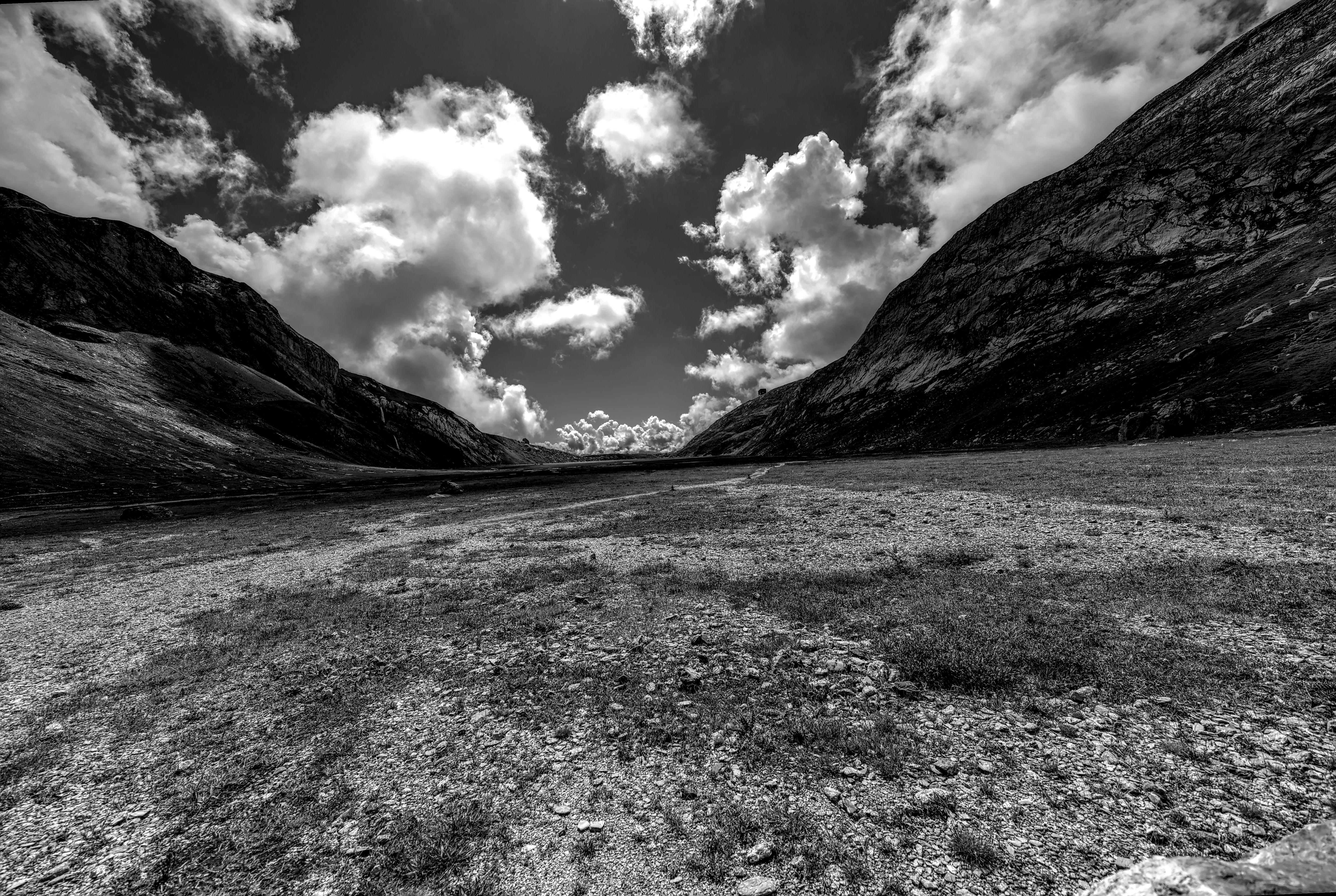A captivating black and white photograph of an alpine valley with dramatic clouds and rugged mountains.