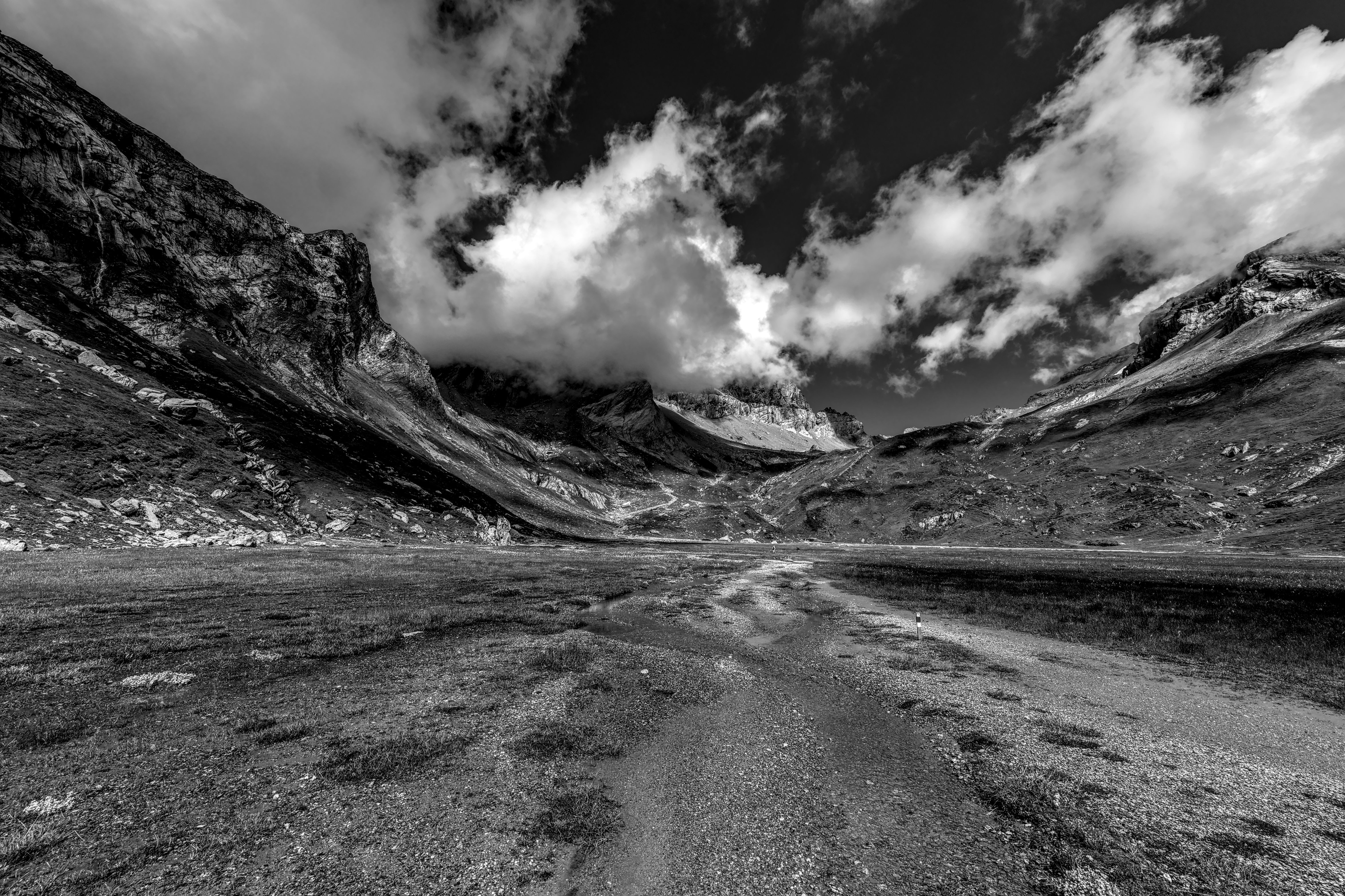 A striking black and white photograph of a mountainous landscape with clouds and rocky terrain.