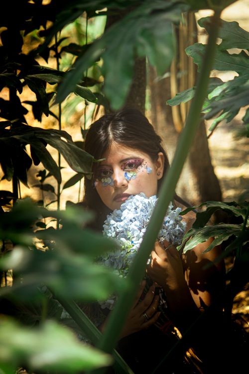 Free A woman in a forest setting with artistic floral makeup holding flowers, captured in warm light. Stock Photo