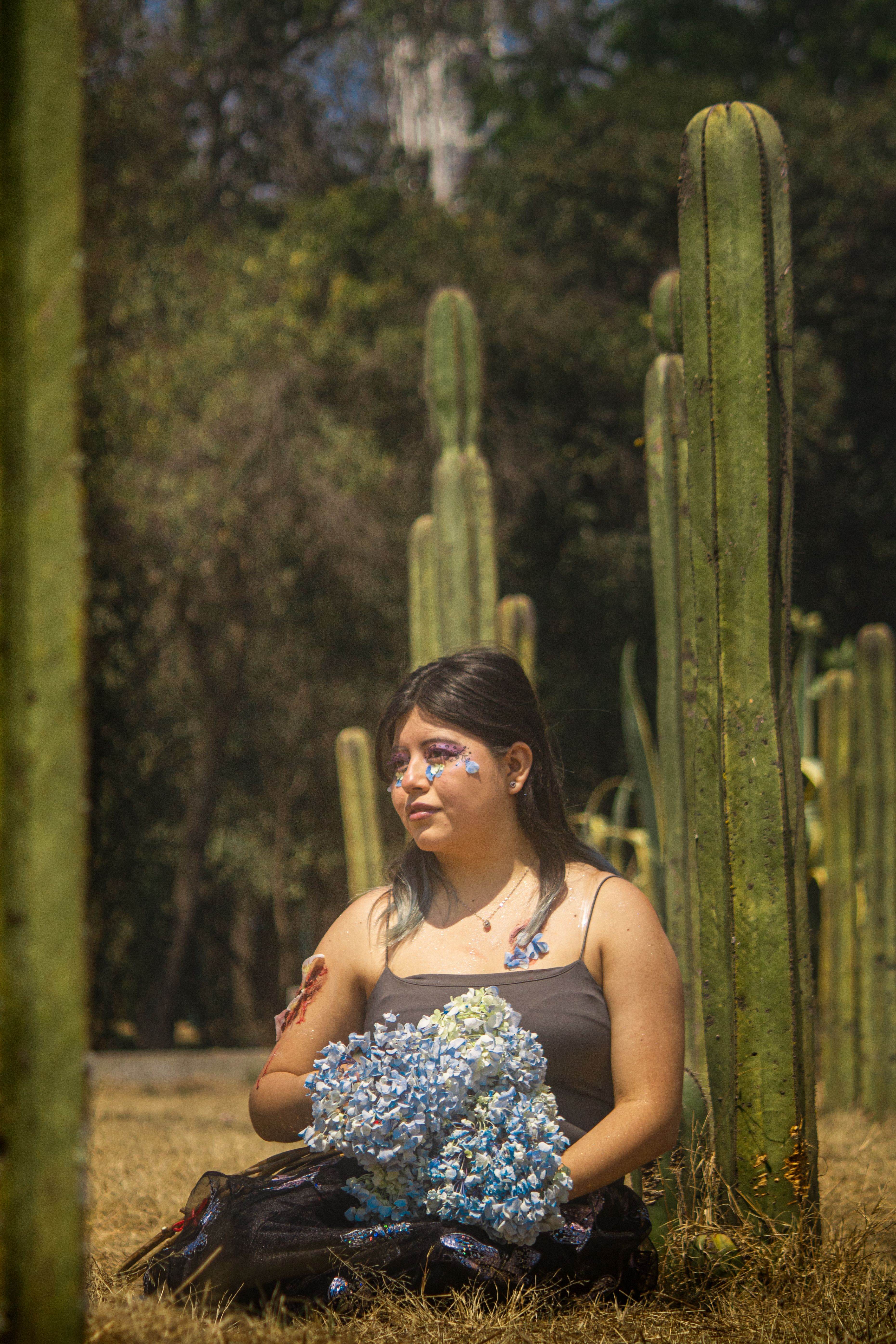 A woman poses with floral makeup among tall cacti, blending art with nature.