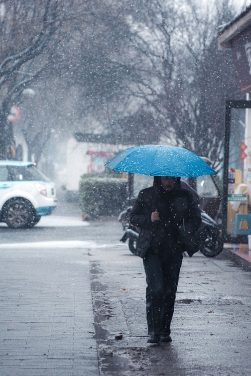Free A person walks down a snowy urban street holding a bright blue umbrella. Stock Photo